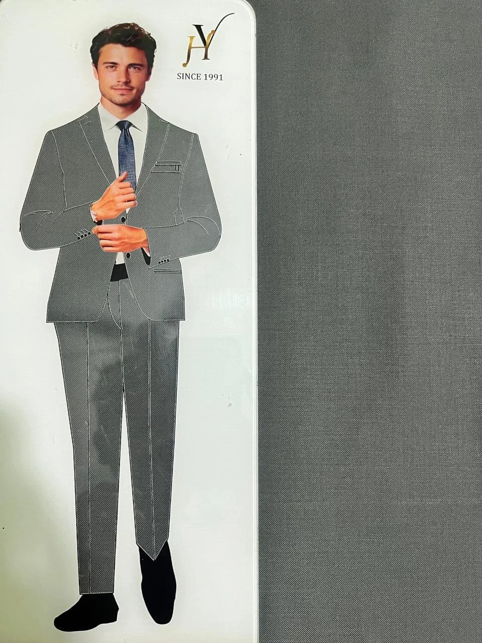 Card with a man wearing a gray suit and tie, next to a gray fabric swatch, with a brand logo on the top right corner.