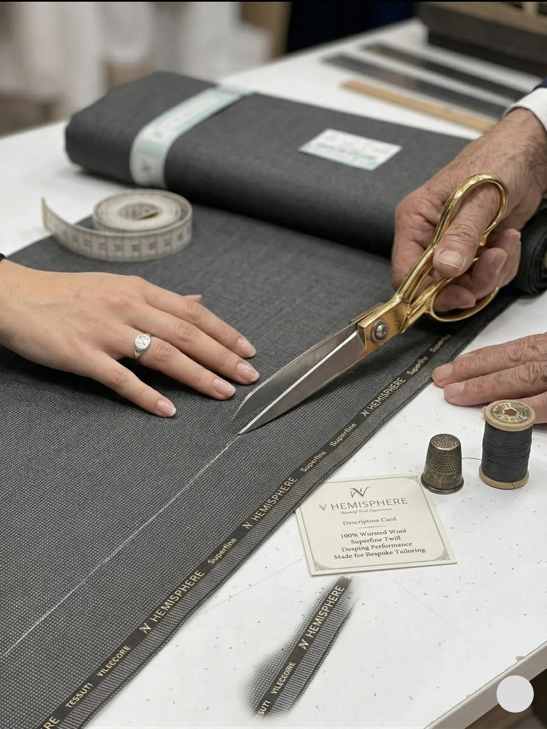 Person cutting gray fabric with scissors on a table with sewing tools.